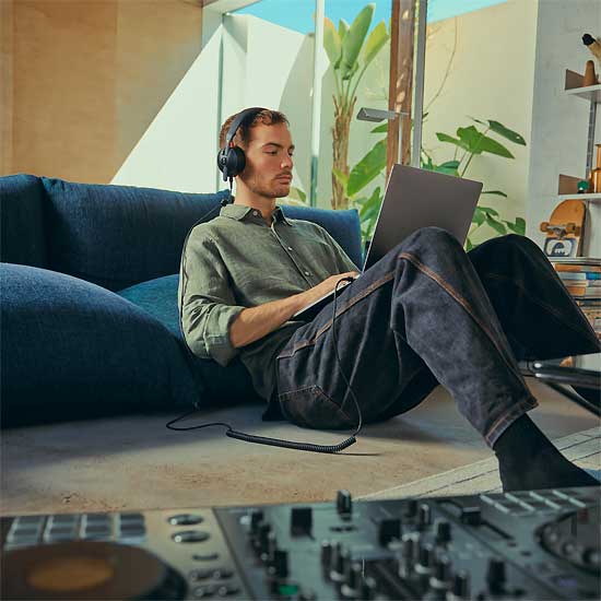 A Man Working on Laptop with NTH-50 Headphones in a Modern Home Studio Setting